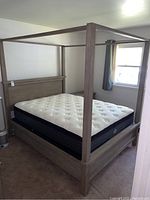 Full view of the queen size four-poster bed frame with mattress in room, showing height, posts, and mattress sitting on frame.