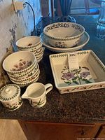 Photo of stacked bowls, square dish, creamer, and sugar bowl showing floral patterns and green leaf border on ceramic dishware