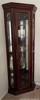 Full view of tall dark wood corner display cabinet with glass door, side glass panels, ornate gold-toned trim, and mirrored back interior with glass shelves.