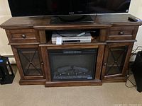 Full front view of dark brown wooden TV cabinet with TV on top, built-in electric fireplace insert, two drawers above, two glass-pane side cabinets
