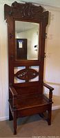 Full front view of the hall tree showing carved crest, mirror, seat, hooks, and base.