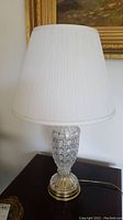 Full view of one table lamp showing the white pleated fabric lampshade and cut glass body with metal base