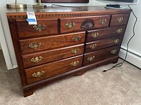 Front view of seven drawer dresser showing drawer arrangement, brass handles, carved shell detail on top center drawer, wood grain finish.