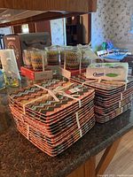 Stack of 32 square zigzag patterned plates, 32 tumblers in original packaging, and a package of 40 Chinet napkins on kitchen counter.
