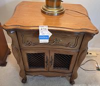 Front view of wooden nightstand with drawer and lower cabinet showing decorative carved details and metal mesh inserts in doors.