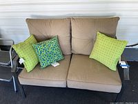 Front view of outdoor sofa with brown cushions, two green dotted pillows and two blue-green patterned pillows.