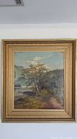 Front view of the oil painting showing the landscape scene with tree, water and mountains inside the ornate wood frame.