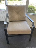 Front view of one patio arm chair showing beige seat and back cushions on a metal frame.