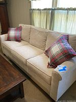 Front three-quarter view of beige sofa with two plaid pillows