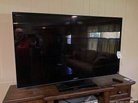 Full view of Sony 55 inch TV on a wooden cabinet with remote control on the side.