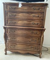 Front view of the tall wooden dresser showing six drawers with decorative carved fronts and ornate metal handles.