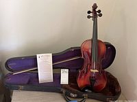Violin and wooden bow inside open black hard case with instruction sheet and lot tag