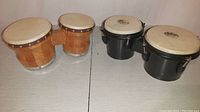 Photo showing both sets of bongo drums on a table, one set natural wood finish the other black painted shells.