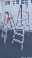 Two aluminum step ladders standing side by side in front of a garage door.