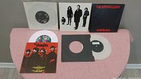 5 The Stranglers 7-inch EP vinyl records arranged on pink cloth surface showing various covers and vinyl colors