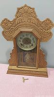 Front view of carved wooden gingerbread clock with intricate floral design and key placed in front.