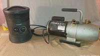 Both items together: Bullet vacuum pump with black motor casing and attached handle, Honeywell heater with two control knobs and air vents.
