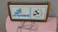 Front view of the full advertising clock showing The Co-operators logo, clock face, wooden frame, and attached power cord on a pink cloth surface.