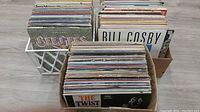 Three boxes containing over 180 LP vinyl records, covers show age wear, with a variety of album covers visible including Bill Cosby and The Beatles.