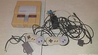 Full lot including SNES console, two controllers, power adapter, and RF switch cable with connectors visible.