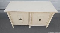 Front view of the white midcentury buffet showing two doors with decorative beaded trim and round metal ring handles.