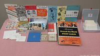 View of the full lot with multiple stamp-related items spread out on a surface including albums, pamphlets, stamp sheets and loose stamps.