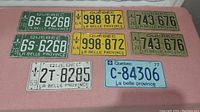 Eight Quebec license plates laid flat, showing three pairs and two singles with various colors and years.