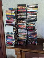 Six uneven stacks of VHS tapes on wooden table, titles visible on spines