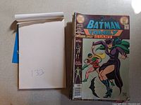 Comic books displayed with Batman Family front cover visible. Notebook with number '133' next to comics.