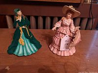 Both porcelain lady figurines placed side by side on wooden surface showcasing full figures and attire.