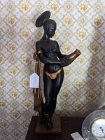 Front view of Toscano resin statue showing black and gold painted African woman holding vessel.