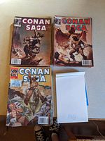 Top view photo showing 3 Conan Saga comic book issues with detailed cover art, accompanied by a small stack of additional comics.