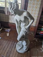 Full side view of the white resin statue of a nude woman crouching, holding fabric.