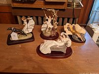 Four Louis Icart limited edition figurines displayed on wood surface. Front piece reclining woman with flowers, girl on swing, woman walking dog, woman seated by tree.