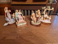 Four porcelain figural groups on a table, showing all groups together, showcasing variety in poses and arrangements.