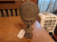 Front view of the African carved wooden fertility figure showing large circular head, closed eyes, earrings, and torso details.