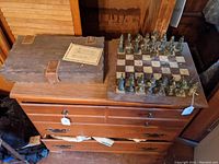 Wide shot showing closed storage box, certificate, chess board and pieces on dresser