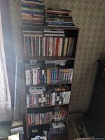 Full view of the tall bookcase packed with martial arts books and VHS tapes on multiple shelves against floral wallpapered wall.