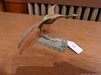 Side view of the brass bird sculpture showing the extended right wing and marble base on a wooden table.