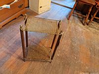 Metal wire stand with two rectangular shelves and round finials at corners. Shows geometric wire pattern and some rust.
