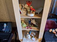 Porcelain figurines displayed on shelves including a seated woman, red birds on branch, clawfoot bathtub, and couples.