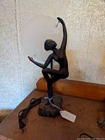 Full side view of the lamp showing the seated nude figure, black finish, plugged in with attached price tag.