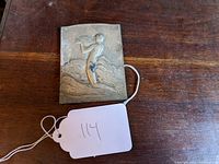 Front view of bronze or metal bas relief plaque depicting a figure blowing a horn.