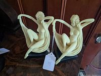 Pair of nude Art Deco Toscano statues seated on dark bases with flowing drapery and posed with one arm behind head and one arm extended holding cloth.