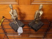 Pair of brass figures seated in a crouching position on black marble bases.