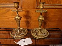 Pair of brass candlesticks on wooden surface showing full height and base design.