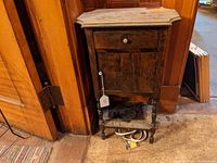 Full front view of vintage wooden tobacco stand with marble top positioned against a wood paneled wall.