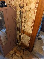 Full view of the vintage solid brass hat and coat rack with multiple curved hooks and round top finial in a room corner