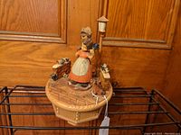 Full view of the vintage Thorens music box showing the carved wooden figurines of a woman and child, birds, dog, and lamp post on a patterned wooden base.