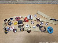 Overall view of the woven beige band with multiple vintage rock and band pin buttons attached showing various designs and artists.
